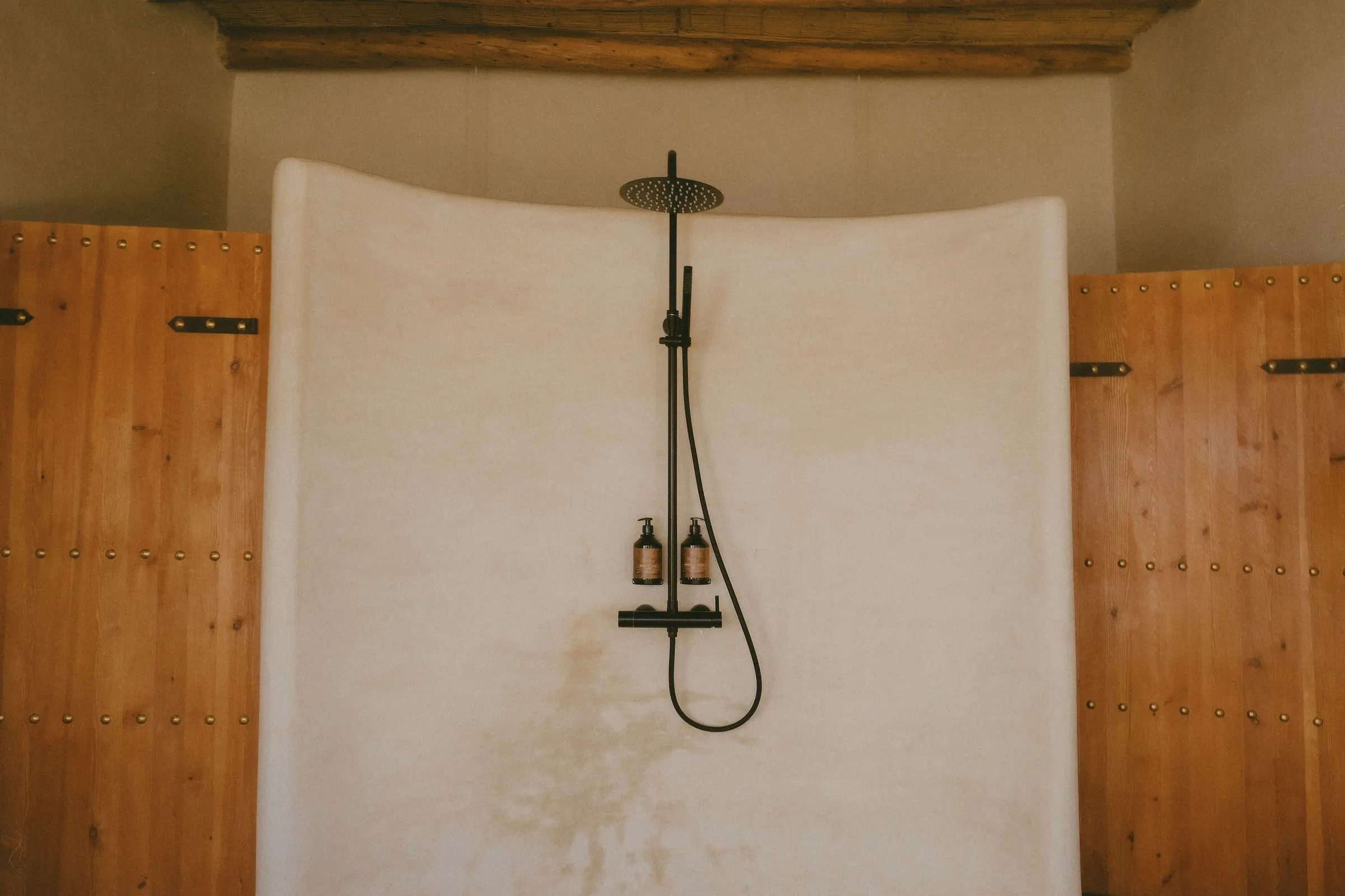 A curved lime-plaster shower wall with a rain shower between wooden doors