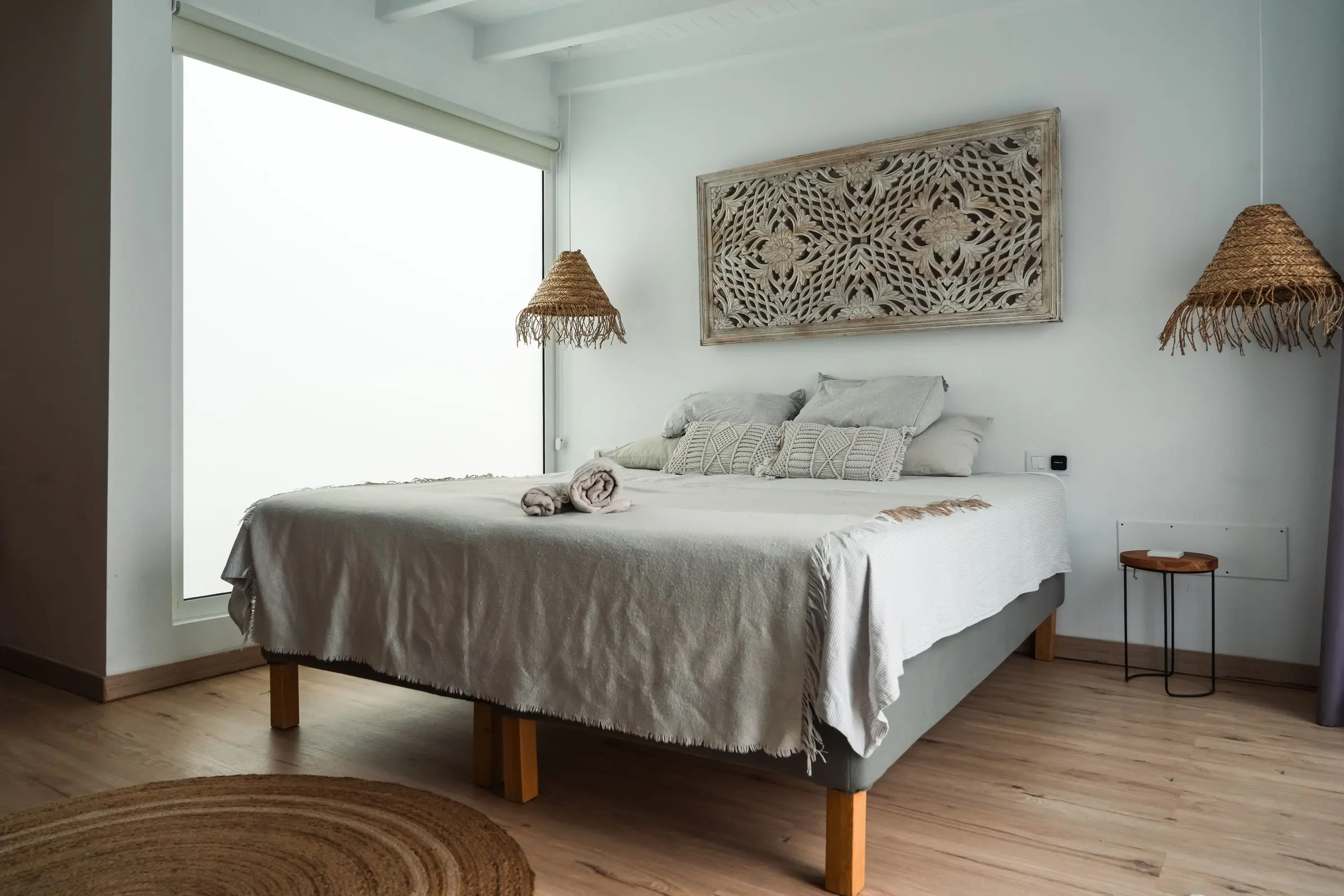 A bright white bedroom with a linen-draped bed and woven raffia pendant lamps