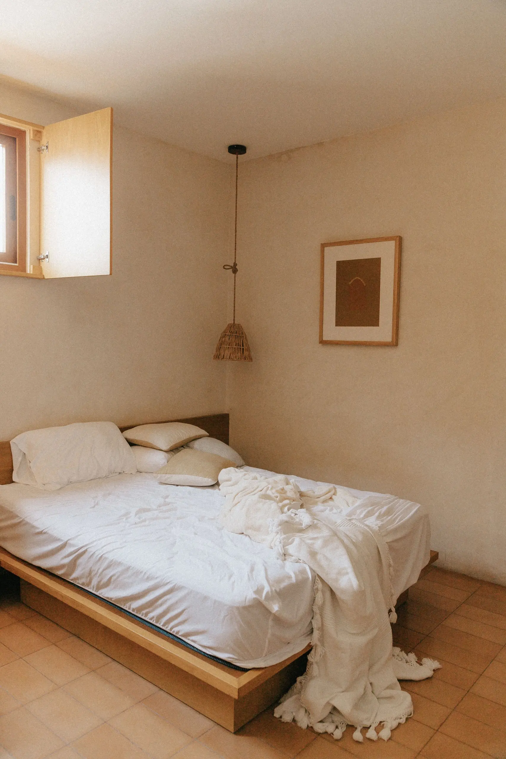 A calm bedroom with warm plaster walls, a low wooden bed and terracotta floor tiles
