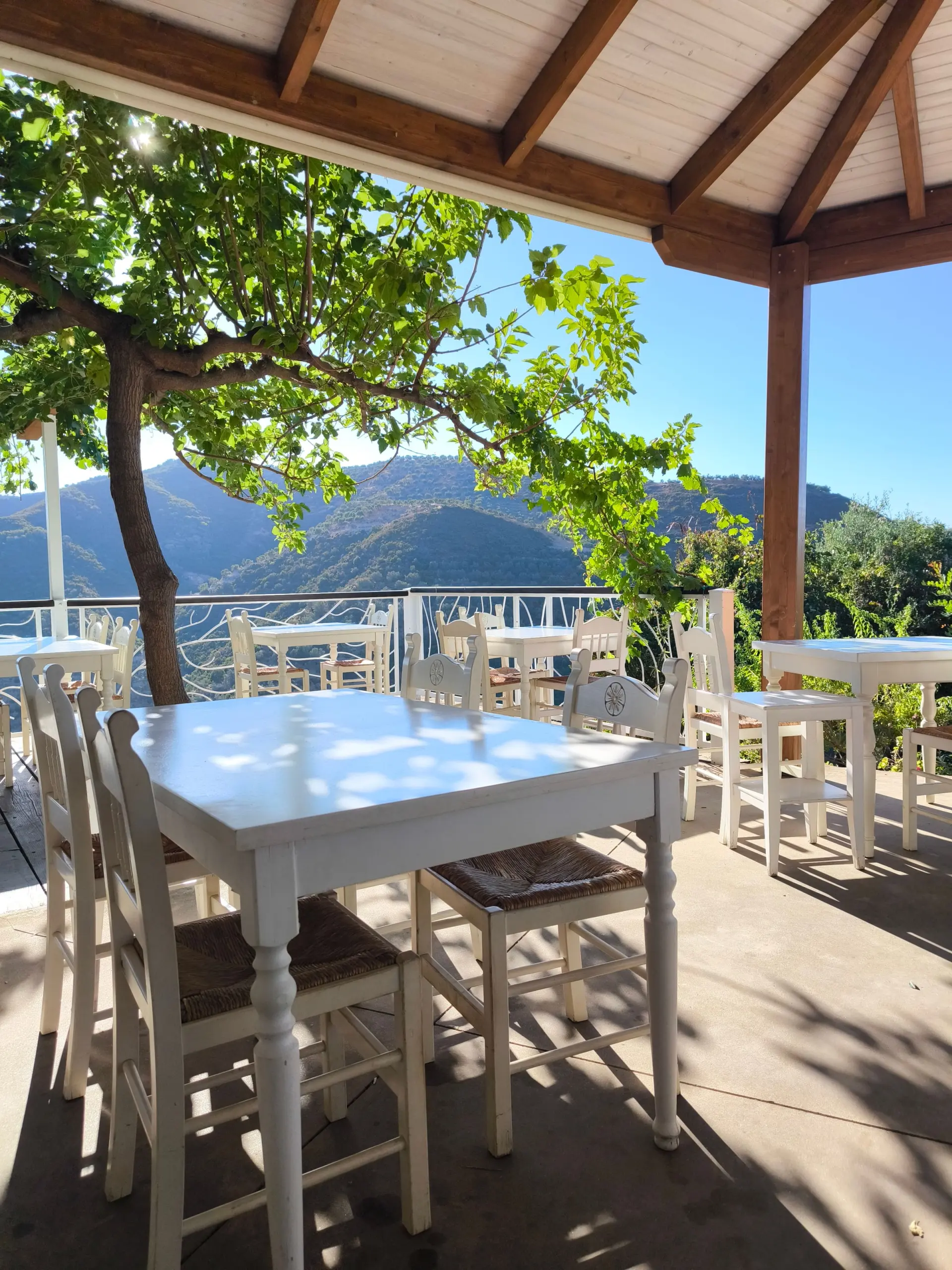 White tables and rush-seat chairs under a timber pergola overlooking green hills