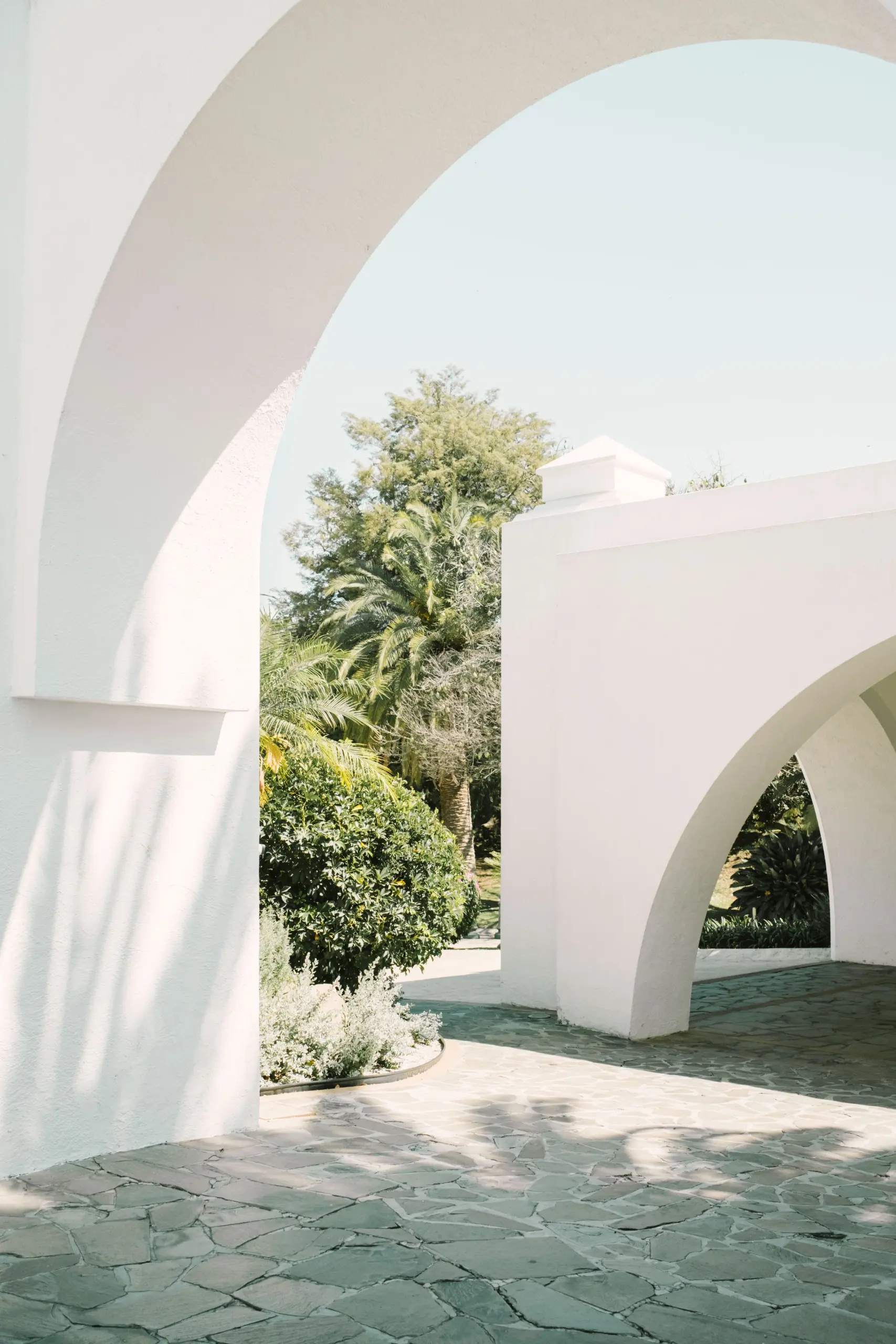 Sunlit white plaster arches opening onto a stone courtyard and a garden of palms