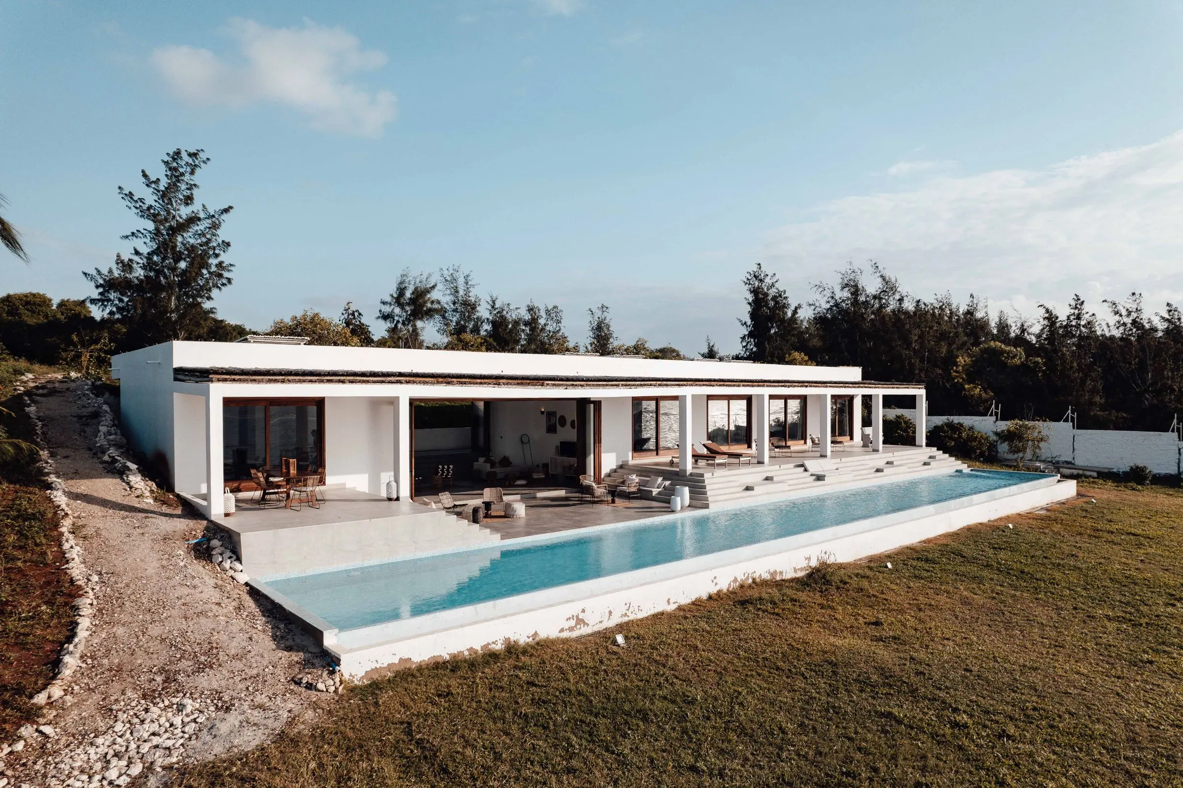A long pool running along a single-storey white villa with a shaded terrace